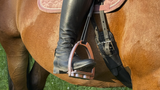 Test strzemion Tech Stirrups Venice Plus Evo – jeźdźczyni na gniadym koniu podczas treningu na odkrytej arenie piaskowej, baloty siana w tle
