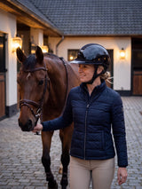 Rider wearing a Samshield Miss Shield 2.0 Night Pearl helmet leading her horse across the stable courtyard at dusk